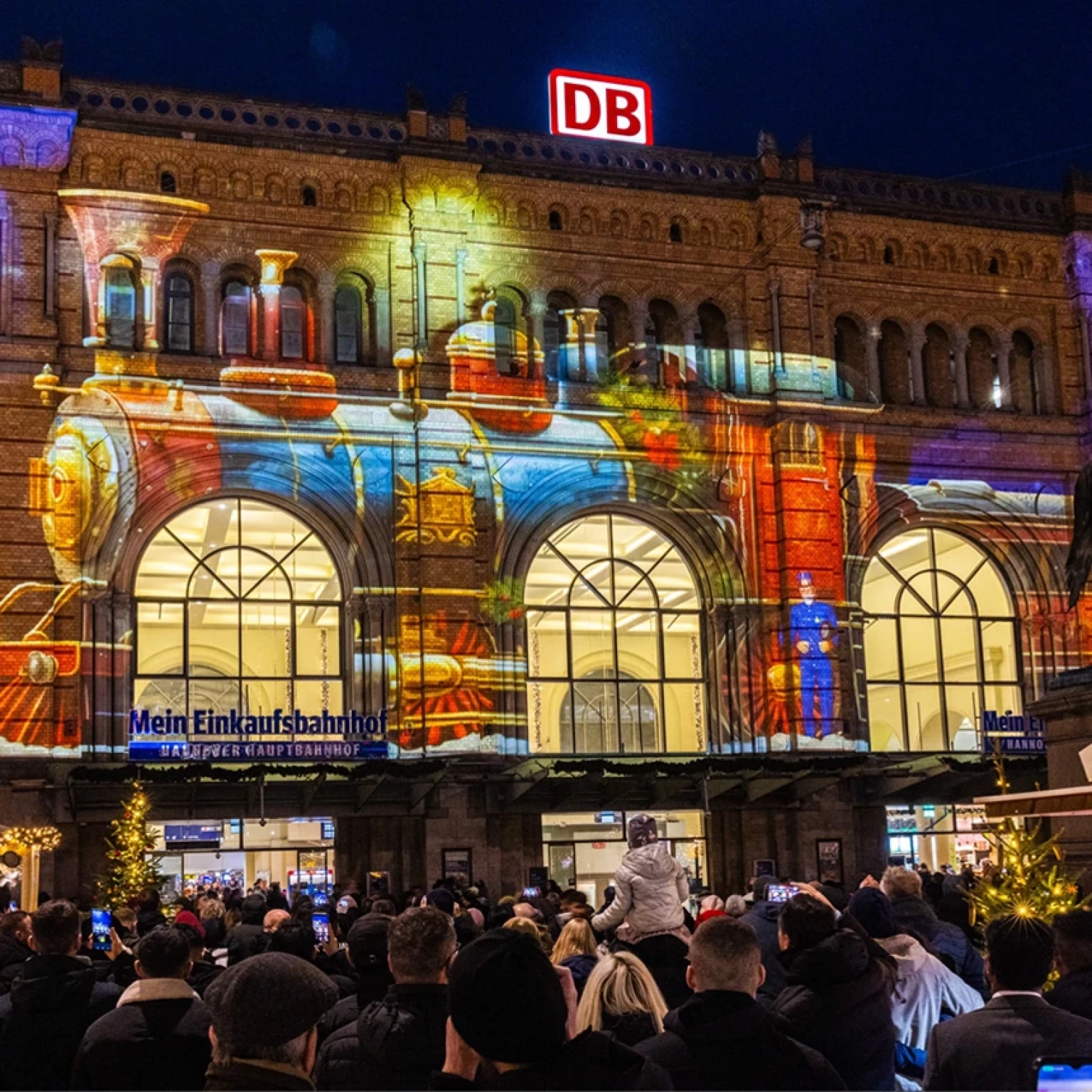 Many people stand in front of the main train station in Hanover and look at a projection on the facade