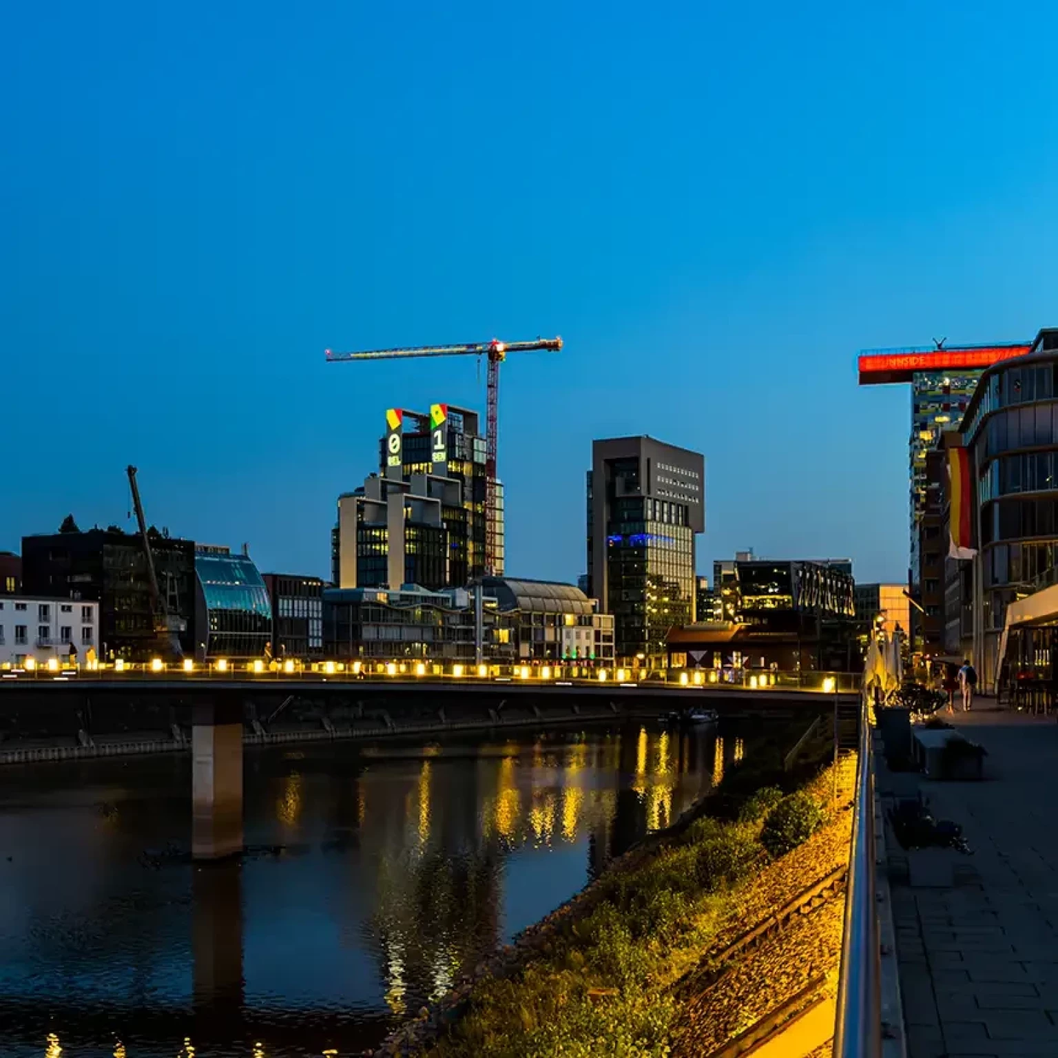UNIQ TOWERS im Düsseldorfer Medienhafen zeigen mit Projectionmapping bei Nacht den Live-Spielstand einer WM-Partie auf der Fassade, im Vordergrund spiegelt sich die Beleuchtung im Wasser des Hafenbeckens.